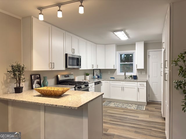 kitchen featuring a peninsula, light wood-style floors, white cabinets, stainless steel appliances, and a sink