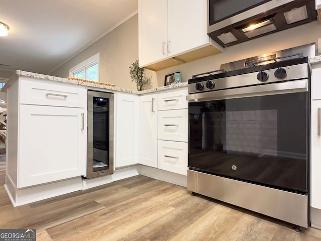 kitchen with light stone countertops, appliances with stainless steel finishes, white cabinetry, wine cooler, and light hardwood / wood-style flooring