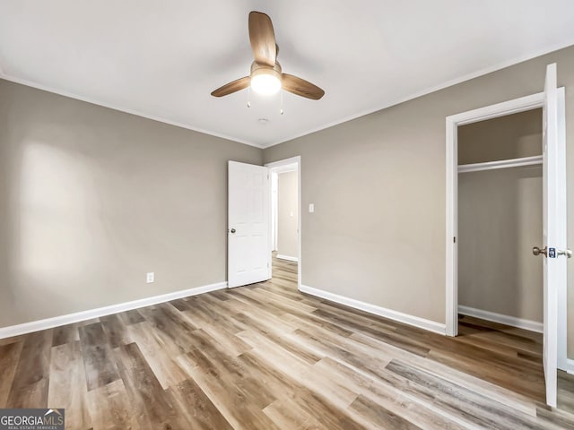 unfurnished bedroom featuring crown molding, baseboards, wood finished floors, a closet, and a ceiling fan