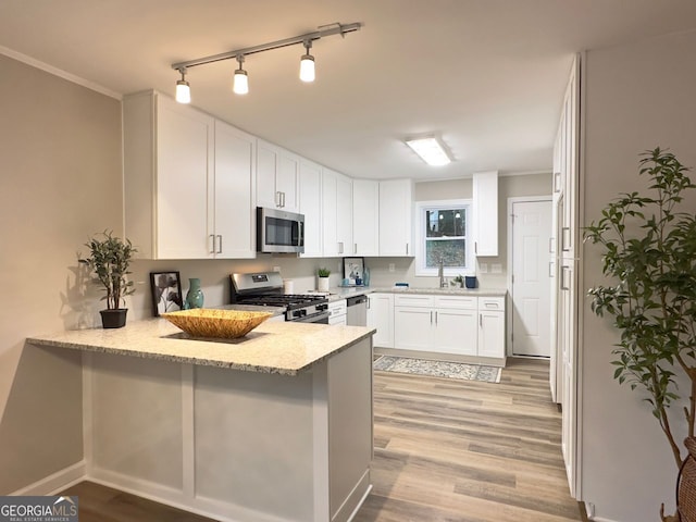 kitchen with white cabinets, appliances with stainless steel finishes, kitchen peninsula, light wood-type flooring, and light stone counters