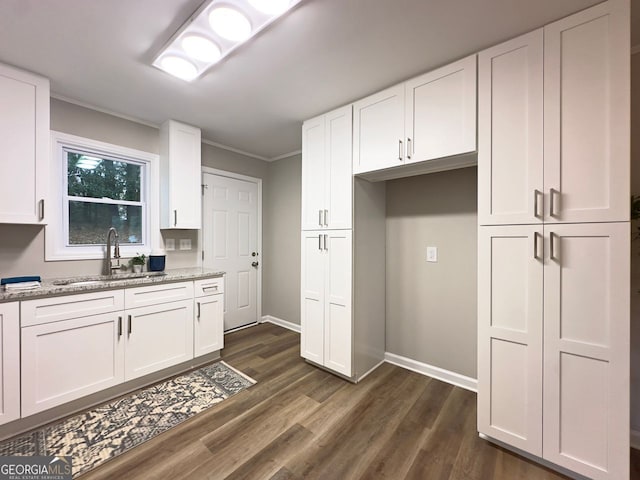 kitchen with light stone counters, dark wood-style floors, ornamental molding, a sink, and white cabinetry