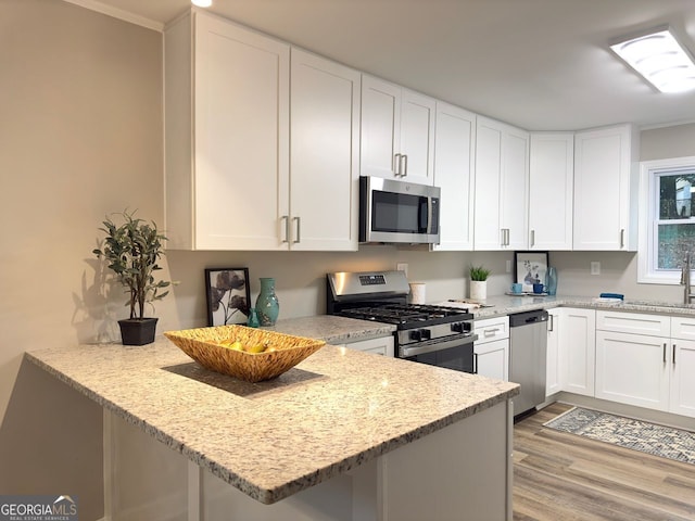 kitchen featuring light stone countertops, light wood-style flooring, a peninsula, white cabinets, and stainless steel appliances