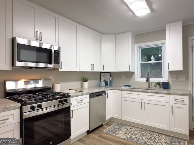 kitchen with a sink, white cabinets, light wood-style floors, and stainless steel appliances