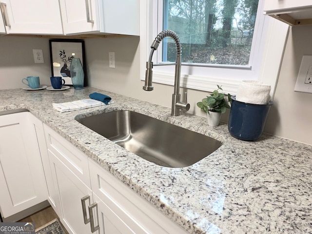 room details with light stone countertops, white cabinetry, and a sink