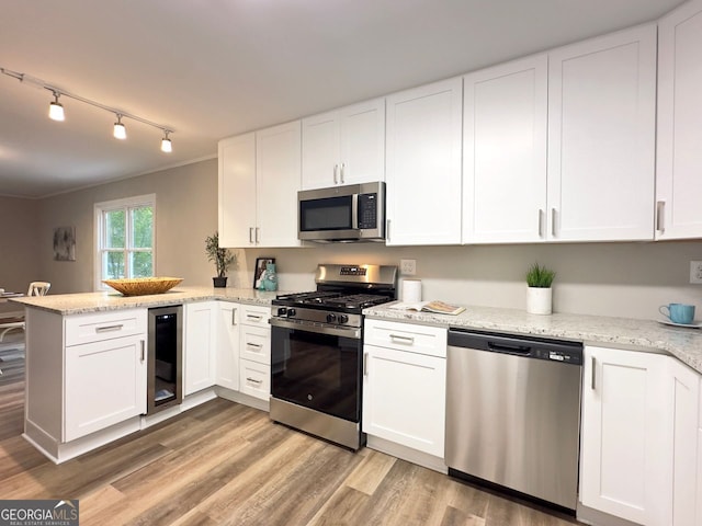 kitchen with beverage cooler, light wood-type flooring, appliances with stainless steel finishes, a peninsula, and white cabinetry