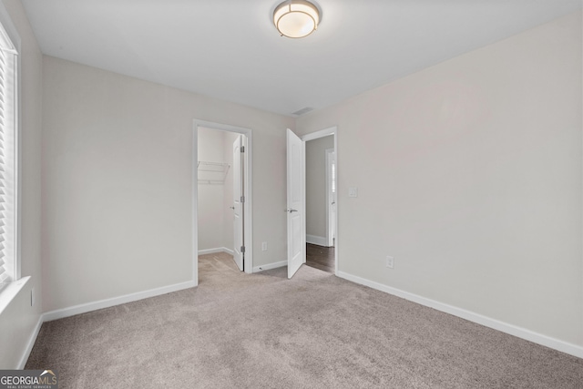 unfurnished bedroom with light colored carpet, a closet, and a spacious closet