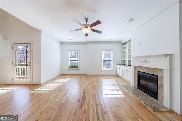 unfurnished living room featuring a premium fireplace, light wood-type flooring, ornamental molding, built in features, and ceiling fan