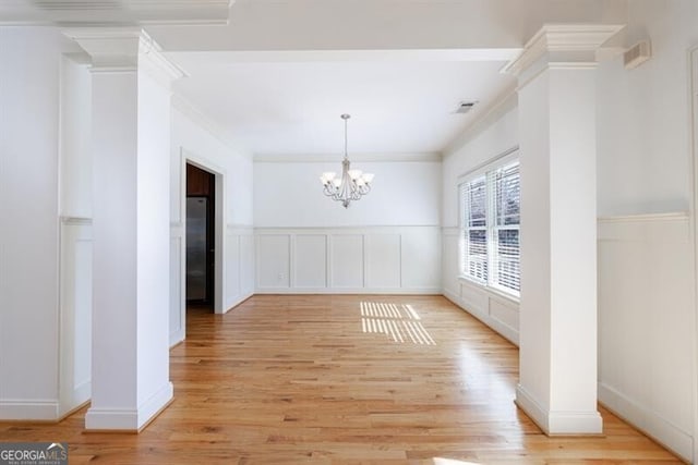 unfurnished dining area with ornate columns, a notable chandelier, ornamental molding, and light hardwood / wood-style floors