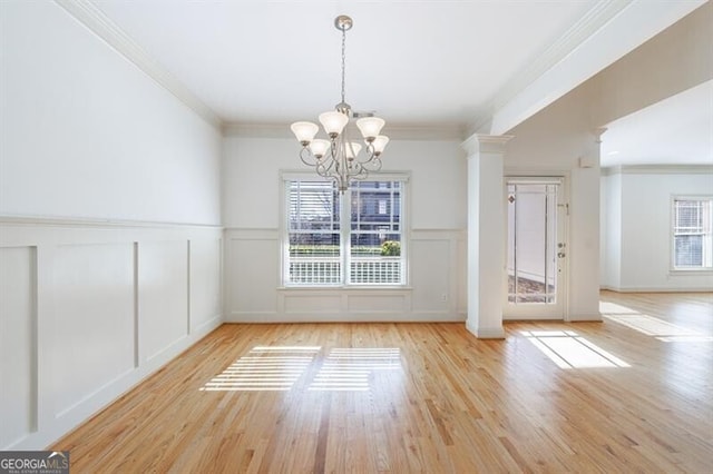 unfurnished dining area with ornate columns, ornamental molding, a chandelier, and light wood-type flooring