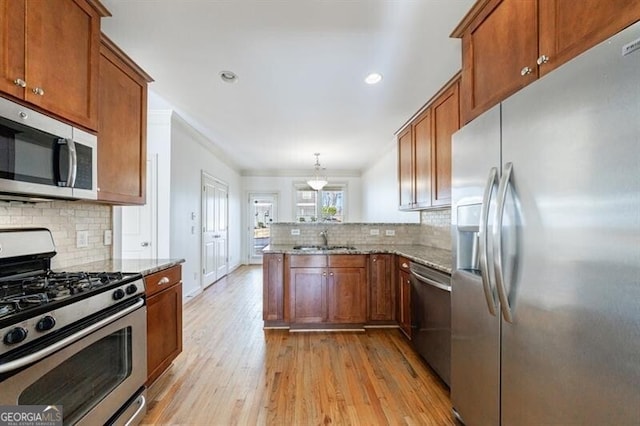 kitchen featuring kitchen peninsula, hanging light fixtures, appliances with stainless steel finishes, sink, and light stone counters