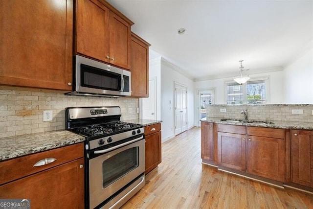 kitchen with light stone countertops, stainless steel appliances, sink, hanging light fixtures, and light hardwood / wood-style flooring