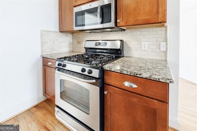 kitchen with light stone counters, light hardwood / wood-style floors, decorative backsplash, and appliances with stainless steel finishes