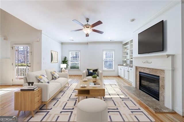 living room with a premium fireplace, built in shelves, crown molding, and light hardwood / wood-style floors