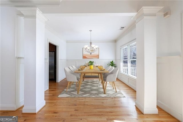 dining space with decorative columns, light wood-type flooring, crown molding, and a notable chandelier