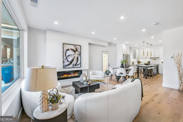 living room featuring light wood-style flooring, recessed lighting, visible vents, baseboards, and a glass covered fireplace