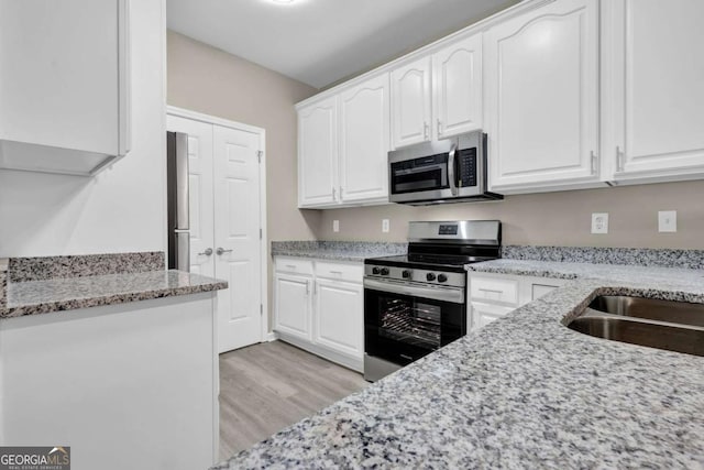 kitchen featuring light hardwood / wood-style flooring, light stone countertops, stainless steel appliances, and white cabinetry