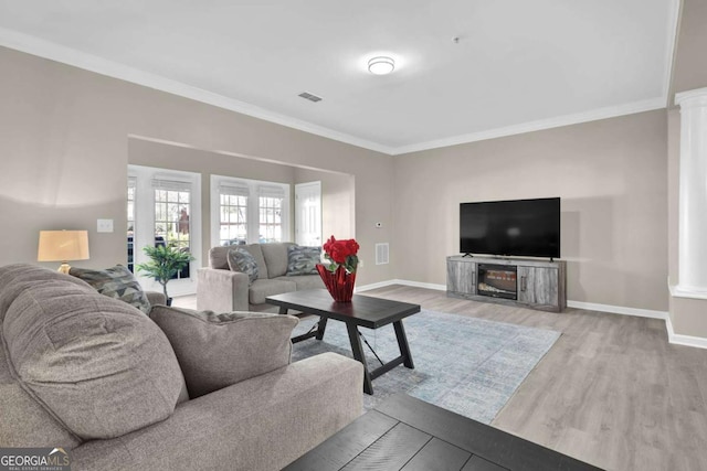 living room featuring a fireplace, ornamental molding, ornate columns, and light wood-type flooring