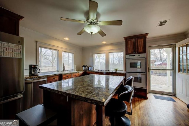 kitchen with a kitchen island, stainless steel dishwasher, a wealth of natural light, sink, and double oven