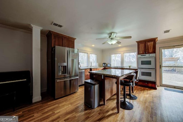 kitchen featuring a kitchen bar, ceiling fan, stainless steel appliances, a kitchen island, and crown molding