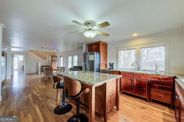 kitchen featuring stainless steel fridge, ceiling fan, light hardwood / wood-style flooring, light stone counters, and a center island