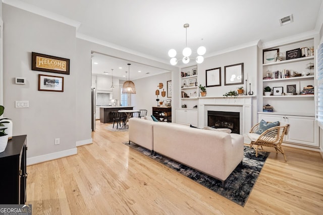 living room featuring ornamental molding, built in features, a chandelier, and light hardwood / wood-style floors