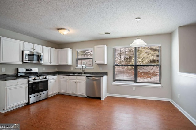 kitchen with white cabinetry, appliances with stainless steel finishes, a healthy amount of sunlight, hanging light fixtures, and sink