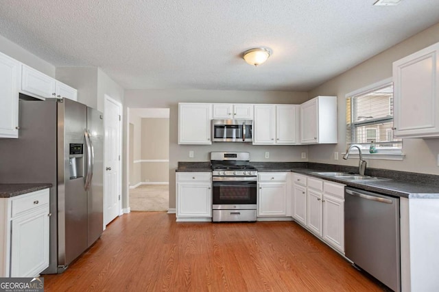 kitchen featuring a textured ceiling, white cabinets, stainless steel appliances, light hardwood / wood-style floors, and sink