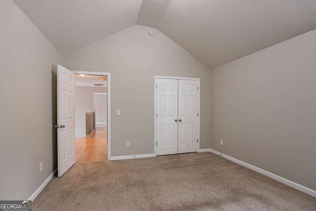 unfurnished bedroom with a textured ceiling, a closet, lofted ceiling, and carpet floors