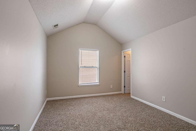 spare room featuring lofted ceiling, carpet floors, and a textured ceiling