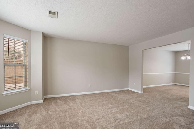 empty room featuring a textured ceiling, a chandelier, and carpet