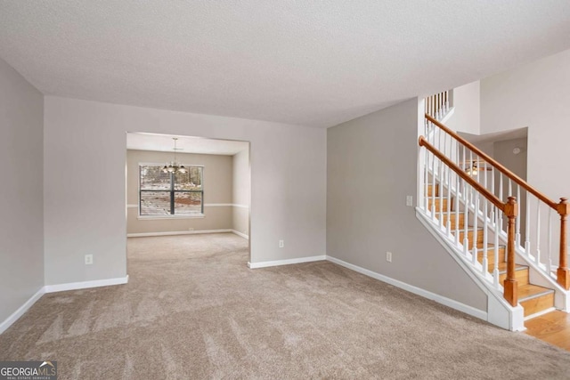 spare room featuring light colored carpet, a textured ceiling, and a notable chandelier