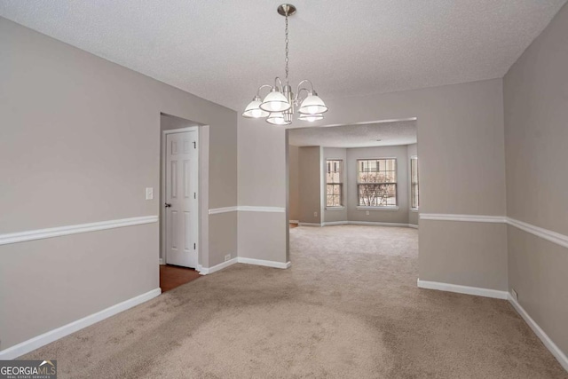 spare room with a textured ceiling, carpet floors, and a notable chandelier