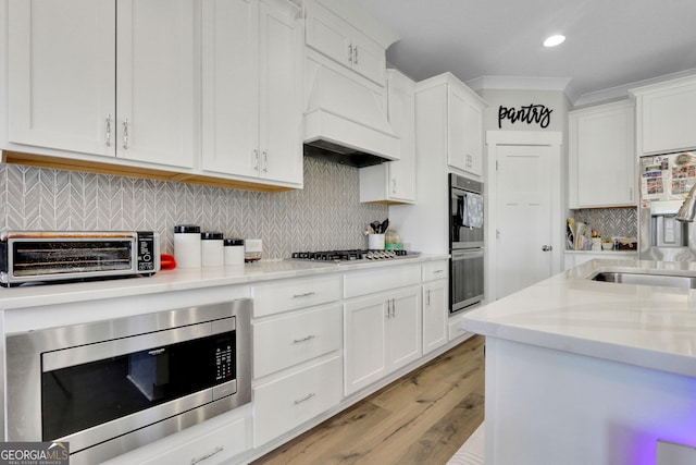 kitchen with stainless steel appliances, light stone counters, ornamental molding, custom range hood, and white cabinets