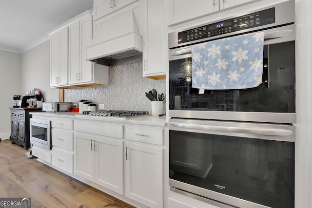 kitchen featuring premium range hood, crown molding, tasteful backsplash, appliances with stainless steel finishes, and white cabinets