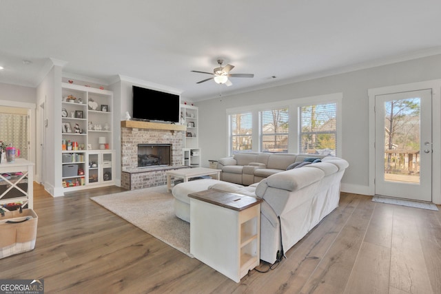 living room featuring hardwood / wood-style flooring, ornamental molding, a brick fireplace, and ceiling fan