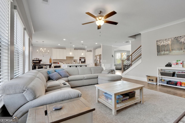 living room featuring hardwood / wood-style flooring, crown molding, and ceiling fan with notable chandelier