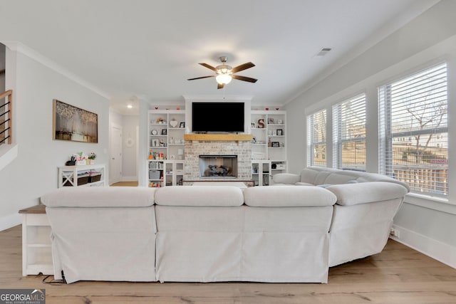 living room featuring ornamental molding, built in shelves, a fireplace, and light hardwood / wood-style floors