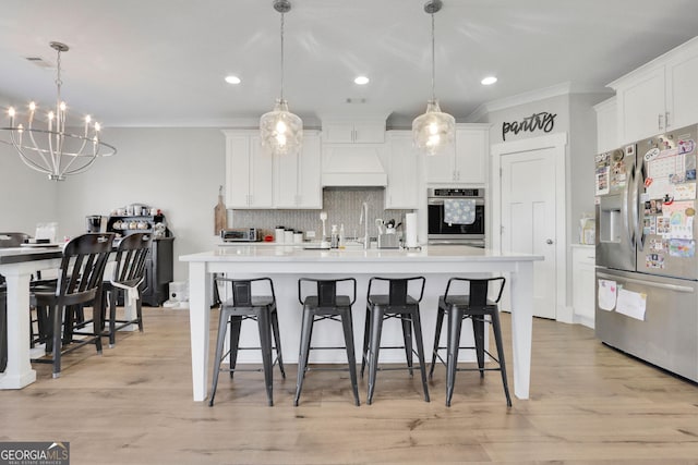 kitchen featuring pendant lighting, premium range hood, white cabinets, and appliances with stainless steel finishes