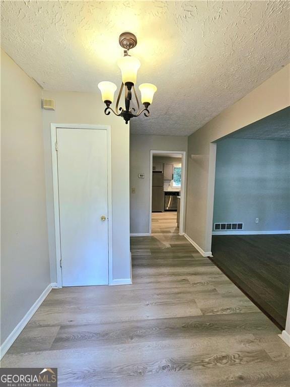 unfurnished room with hardwood / wood-style floors, a textured ceiling, and a notable chandelier