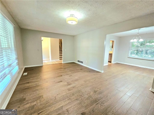 unfurnished room with wood-type flooring, an inviting chandelier, and a textured ceiling