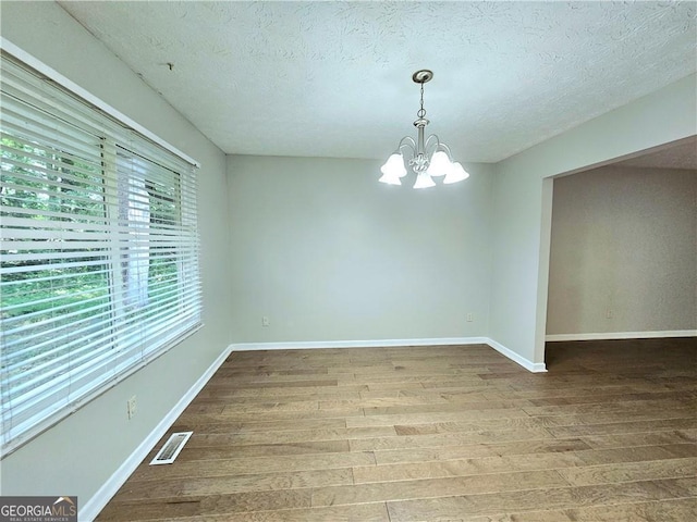 unfurnished room with a textured ceiling, a chandelier, and hardwood / wood-style floors