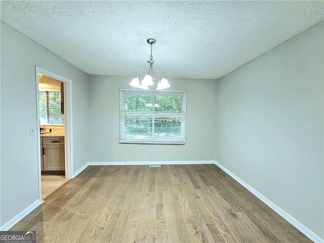 unfurnished dining area with hardwood / wood-style flooring, a textured ceiling, and a notable chandelier