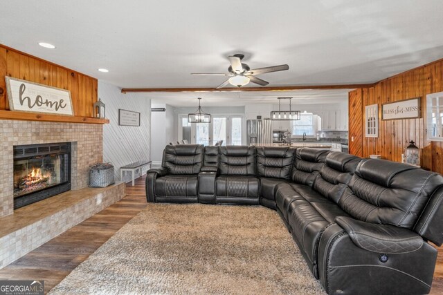 living room featuring ceiling fan with notable chandelier, dark wood-type flooring, wooden walls, sink, and a tile fireplace