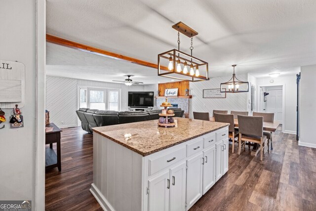 kitchen with ceiling fan with notable chandelier, pendant lighting, a center island, white cabinetry, and wood walls