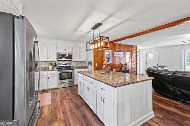 kitchen with appliances with stainless steel finishes, hanging light fixtures, beam ceiling, white cabinets, and a center island