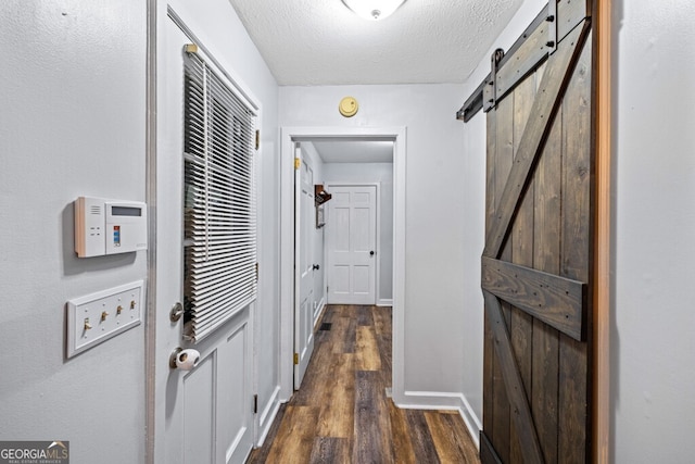 corridor featuring a barn door, dark wood-type flooring, and a textured ceiling