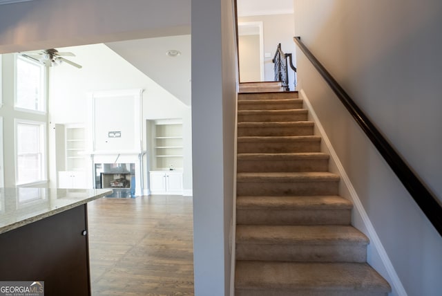 stairway featuring ceiling fan, built in shelves, and a premium fireplace