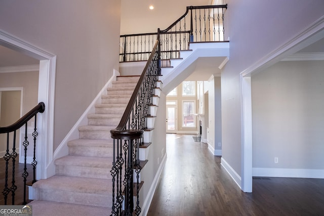 stairway featuring hardwood / wood-style floors, ornamental molding, and a towering ceiling