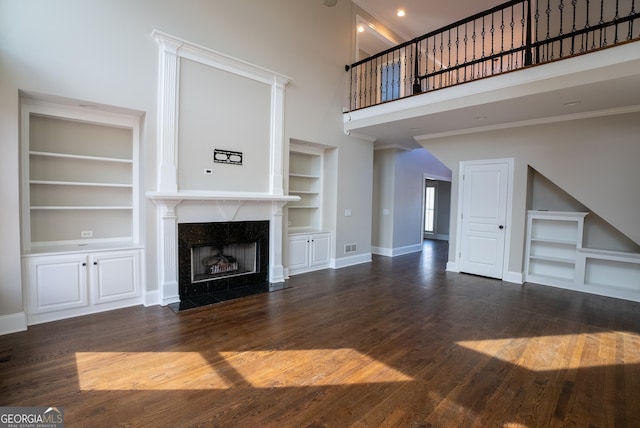 unfurnished living room with dark hardwood / wood-style floors, a fireplace, built in features, and a high ceiling