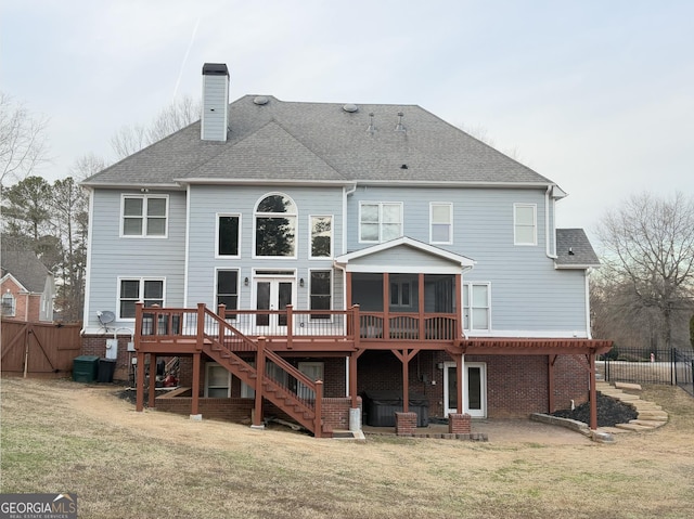 rear view of property featuring a deck, a sunroom, and a lawn